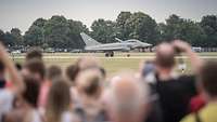Viele Besucher beobachten ein Kampfflugzeug Eurofighter auf der Startbahn.