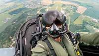Ein Pilot sitzt im Cockpit eines Flugzeuges. Das Flugzeug ist in der Luft.