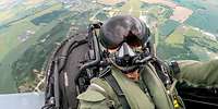 Ein Pilot sitzt im Cockpit eines Flugzeuges. Das Flugzeug ist in der Luft.