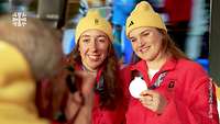 Zwei Sportlerinnen lassen sich mit ihren Medaillen von einer Person fotografieren.