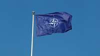A blue flag with the NATO emblem against a blue sky