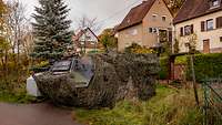 A tank camouflaged with a net is parked in a front garden.