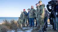 Boris Pistorius und mehrere Soldaten stehen am Strand in den Dünen und beobachten etwas.