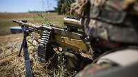 Ein Soldat liegt im Gelände und zielt mit einem Maschinengewehr MG5, das ein Kaliber von 7,62 mm hat.