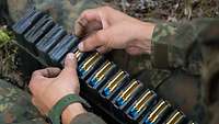 Übungsmonition: Ein Soldat legt blau-goldene Patronen in Magazine.