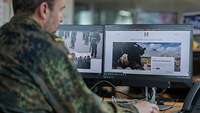 Ein Soldat arbeitet am Computer und schaut auf zwei Bildschirme.