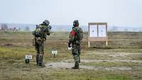 Ein Soldat schießt auf eine Schützenscheibe im Gelände. Ein Soldat steht daneben.