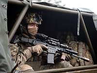 Aus dem hinteren Bereich eines Gefechtsfahrzeugs blickt ein sitzender Soldat mit einer Waffe.