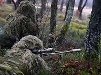 Im Wald liegen zwei spanische Soldaten mit einem Scharfschützengewehr in Stellung. 