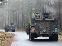 In einem Wald fahren zwei GTK Boxer über eine nasse Asphaltstraße.