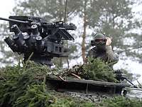 In einem Wald blickt ein stehender Soldat aus der Luke eines getarnten GTK Boxer.