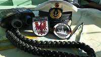 Eine Marinemütze, ein Fernglas und zwei Patches auf einer Seekarte.