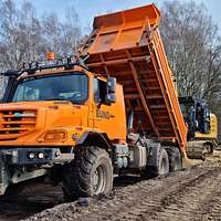 Ein organgefarbender Lastwagen mit abgekippter Ladefläche auf einem Feldweg