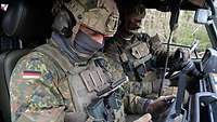 Zwei Soldaten sitzen in einem Fahrzeug, einer bedient einen Kontroller für eine Aufklärungsdrohne.