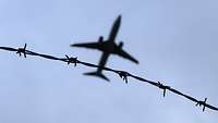 Ein Flugzeug fliegt am Himmel, gesehen von unten durch einen Stacheldraht.