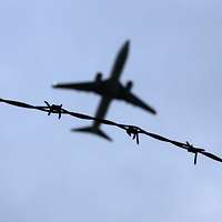 Ein Flugzeug fliegt am Himmel, gesehen von unten durch einen Stacheldraht.