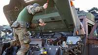Ein Soldat kniet an der Motorhaube eines Fahrzeuges und misst den Ölstand.