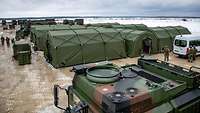 Mehrere Zelte der Bundeswehr in winterlicher Landschaft, dazwischen Fahrzeuge und Soldaten.