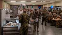 Soldatinnen und Soldaten sitzen an Tischen, frühstücken oder packen sich Lebensmittel in eine Tüte.