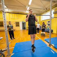 Ein junger Mann hängt an einer Klimmzugstange in einer Turnhalle.
