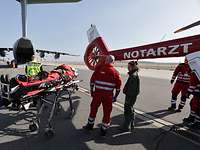 Ziviler Rettungsdienst mit einem Patienten auf einer Trage, im Hintergrund ein Flugzeug