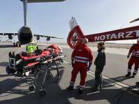 Ziviler Rettungsdienst mit einem Patienten auf einer Trage, im Hintergrund ein Flugzeug