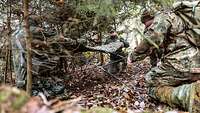 Mehrere Soldaten bauen ein Versteck aus Stangen und einer Plane im Wald.