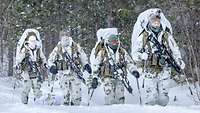 Soldaten in Schneetarn bewegen sich bei Schneefall durch tiefen Schnee.