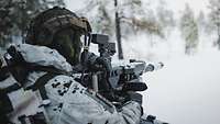 Soldat im Schneetarn zielt mit einer Granatmaschinenwaffe im verschneiten Wald.