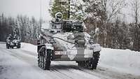 Schneegetarnte Gefechtsfahrzeuge fahren auf einer verschneiten Straße.