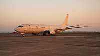 Ein Flugzeug vom Typ P-8A Poseidon steht auf einer asphaltierten Fläche bei tiefstehender Sonne.