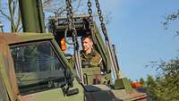 Ein Soldat sitzt in einem grünen Feldkran. Damit hebt er einen Pkw an.