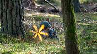 Ein Soldat liegt neben einem Baum und schießt. Helles Mündungsfeuer flammt auf.