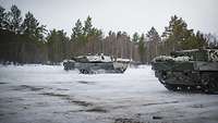 Norwegische Kampfpanzer Leopard 2 fahren über eine verschneite Fläche im Wald.