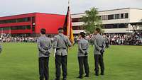 Drei Soldaten und eine Soldatin stehen auf einer Wiese mit der Truppenfahne nebeneinander.
