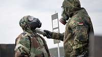 Ein deutscher Soldat hält ein Messgerät an die ABC-Maske eines spanischen Soldaten.