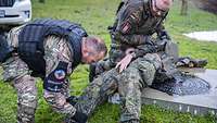 Ein deutscher und ein französischer Soldaten tasten einen deutschen Soldaten nach Verletzungen ab.