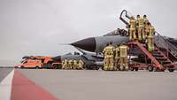 Feuerwehrkräfte stehen in Gruppen an Tornado-Kampfjets und beobachten Soldaten bei der Einweisung.
