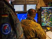 Ein Soldat mit Kopfhörer sitzt vor mehreren Bildschirmen.