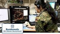 Eine Soldatin mit Kopfhörer sitzt vor mehreren Bildschirmen.