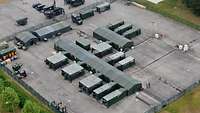 Luftaufnahme von Containern, Zelten und Fahrzeugen, die auf einer asphaltierten Fläche stehen.
