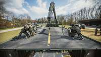 Zwei Soldaten knien auf einem Brückenelement mit Fahrbahn und entfernen die Halteketten vom Kran.