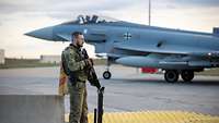 Ein Objektschützer steht bewaffnet vor einem Eurofighter