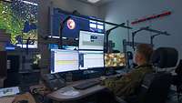 A soldier sits at a workstation in front of several monitors.