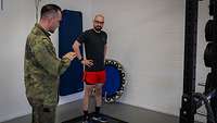 Ein Soldat steht in Sportbekleidung auf einer Messplatte und wird von einem Soldaten angeleitet.
