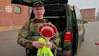 Ein Soldat mit Haltekelle und Warnweste in der Hand steht vor einem Fahrzeug.