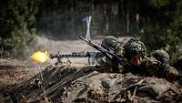Mehrere Soldaten liegen in einer Stellung und schießen. An einer Waffe blitzt Mündungsfeuer auf.