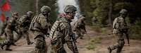 Mehrere Soldaten rennen durch ein bewaldetes Gebiet.