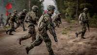 Mehrere Soldaten rennen durch ein bewaldetes Gebiet.