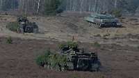 Drei Panzer fahren im Gelände.